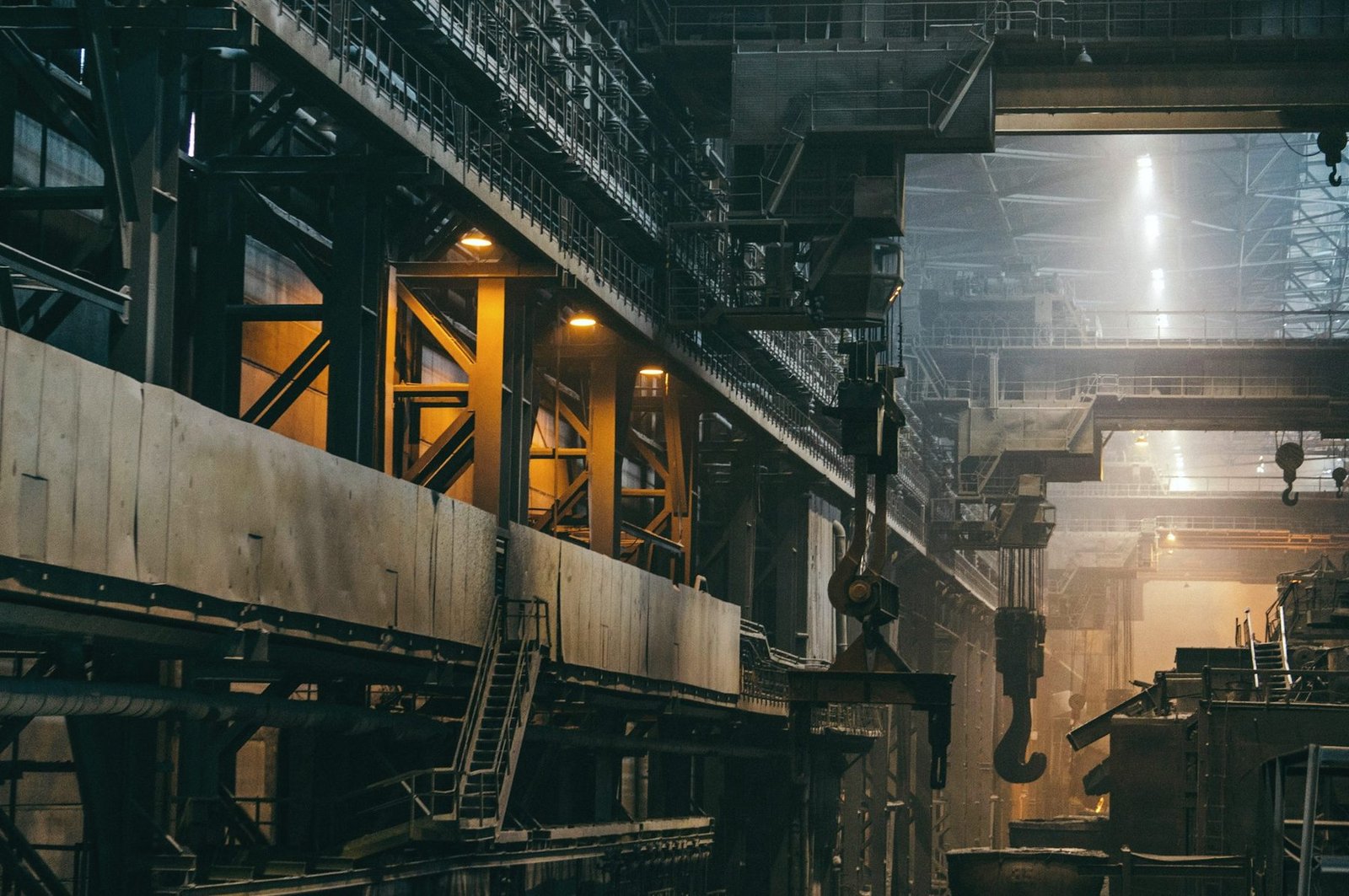 A dim mill interior with heavy steel columns, walkways and light falling through the roof