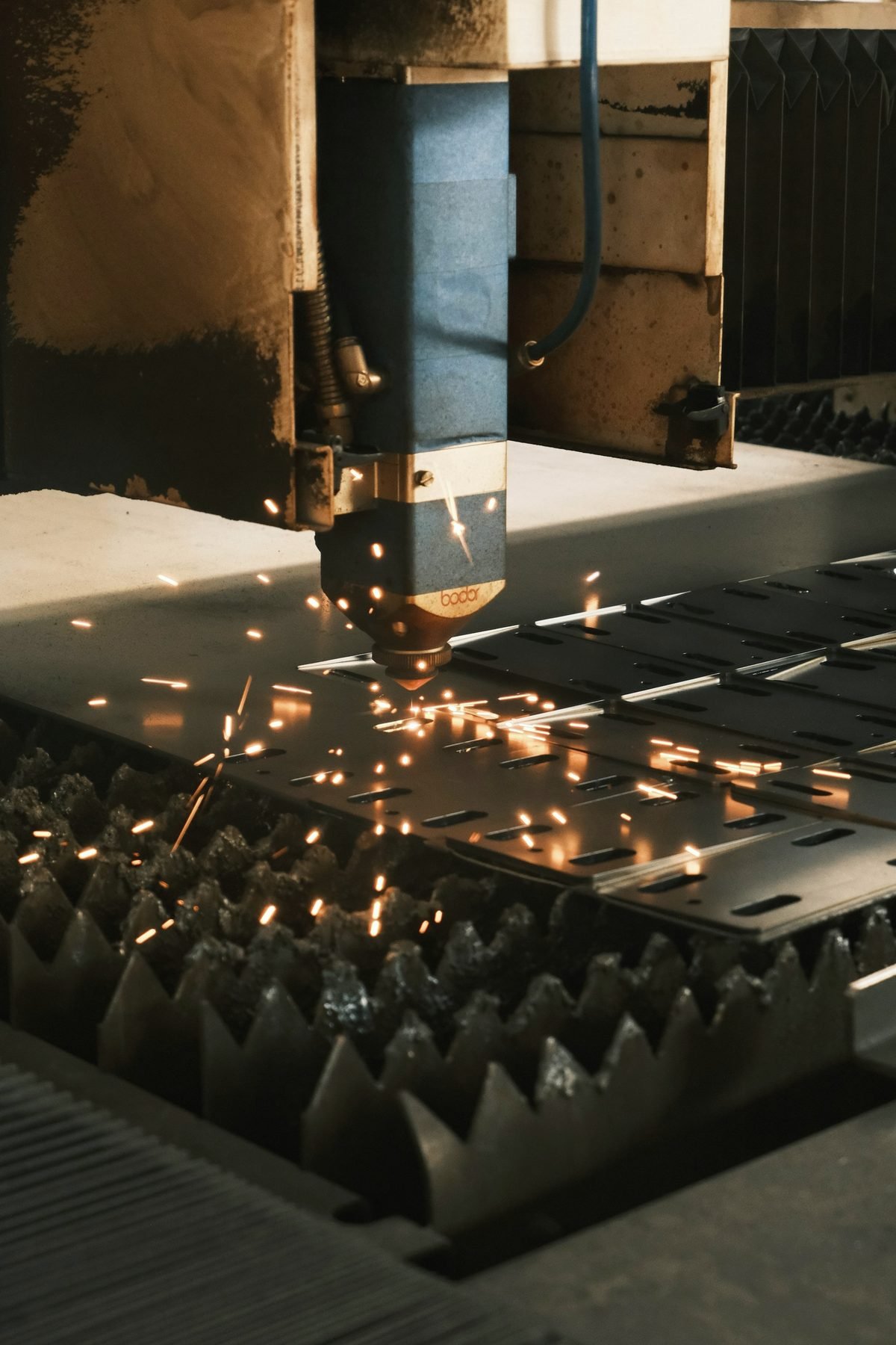 A cutting head working across a steel sheet on a slatted cutting table, sparks dropping below