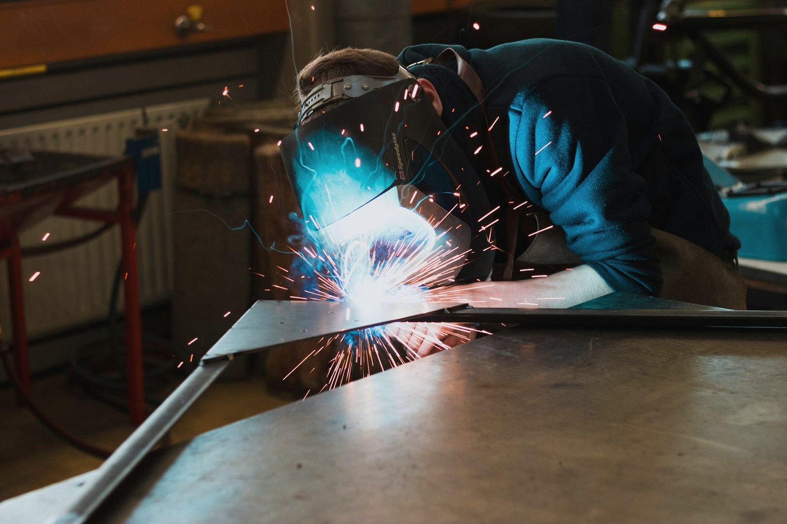 A welder leaning over a large steel plate on a table, welding along its edge